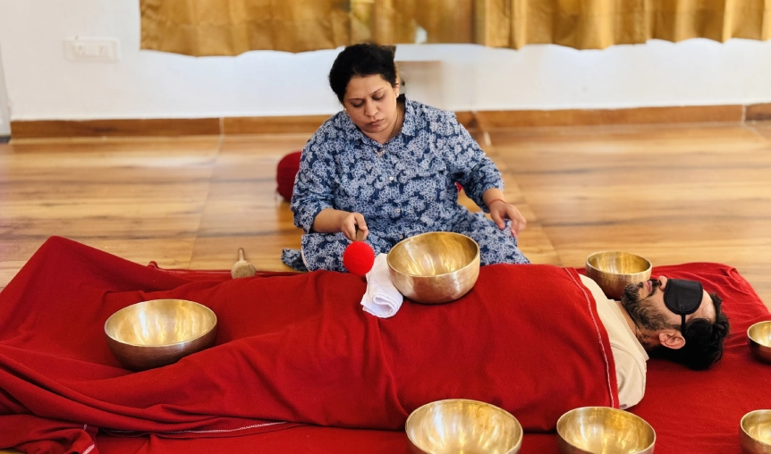 Therapist playing singing bowls around resting student during sound bath session